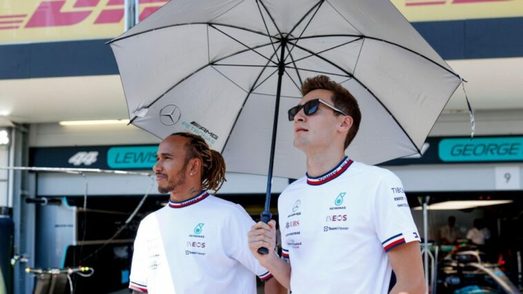 Los compañeros de equipo de Mercedes, Lewis Hamilton y George Russell, de pie bajo un paraguas.  Azerbaiyán, junio de 2022.