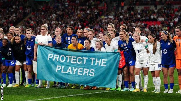 Inglaterra y Estados Unidos sostienen una pancarta que dice proteger a los jugadores