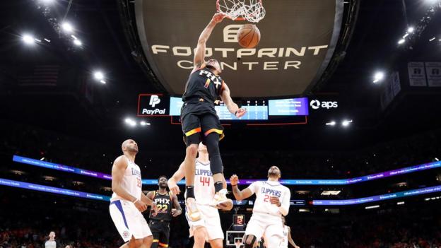 Devin Booker mojando la pelota con tres jugadores de Los Angeles Clippers mirando