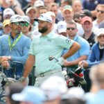 El campeón reinante de Masters mejor clasificado, Jon Rahm, en el centro, espera junto al caddie Adam Hayes durante una ronda de práctica en Oak Hill para el 105.° Campeonato de la PGA.