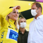 Annemiek van Vleuten bloquea el sol de sus ojos mientras sonríe.  Christian Prudhomme y Marion Rousse aparecen borrosos en el fondo.