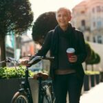 Mujer camina al lado de la bicicleta con un café en la mano.