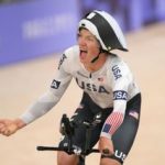 Elouan Gardon conduce su bicicleta de contrarreloj con una mano en la barra de base mientras celebra con el puño con la otra. Lleva una camiseta aerodinámica de manga larga blanca del equipo de EE. UU. y un casco aerodinámico blanco y negro.