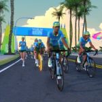 Una captura de pantalla de ciclistas de Zwift en una carretera pavimentada con un arco azul del Tour de Watopia detrás de ellos.