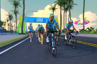 Una captura de pantalla de ciclistas de Zwift en una carretera pavimentada con un arco azul del Tour de Watopia detrás de ellos.