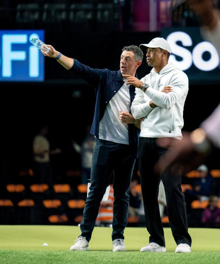 Rory McIlroy y Tiger Woods observan el campo mientras los golfistas se calientan para el partido de golf inaugural en SoFi Center, sede de TGL, la liga de golf interactiva fundada por Tiger Woods y Rory McIlroy el 7 de enero de 2025 en Palm Beach Gardens, Florida.