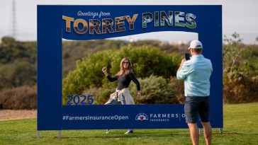 Los fanáticos toman fotos con un letrero de torneo durante la tercera ronda de los 2025 Farmers Insurance Open en Torrey Pines.