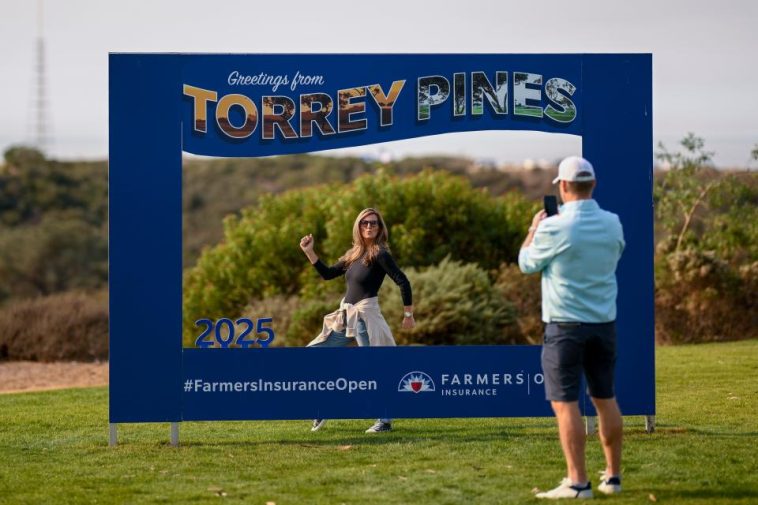 Los fanáticos toman fotos con un letrero de torneo durante la tercera ronda de los 2025 Farmers Insurance Open en Torrey Pines.