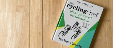 Una copia de The Cycling Chef Plant-Powered Performance sobre una superficie de trabajo de madera clara