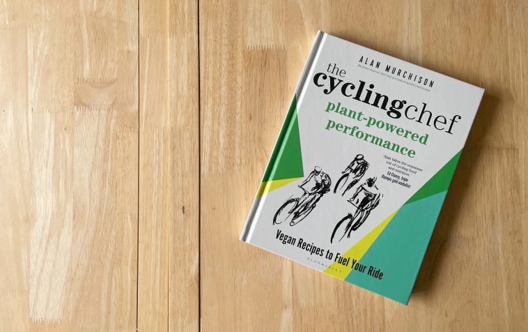 Una copia de The Cycling Chef Plant-Powered Performance sobre una superficie de trabajo de madera clara